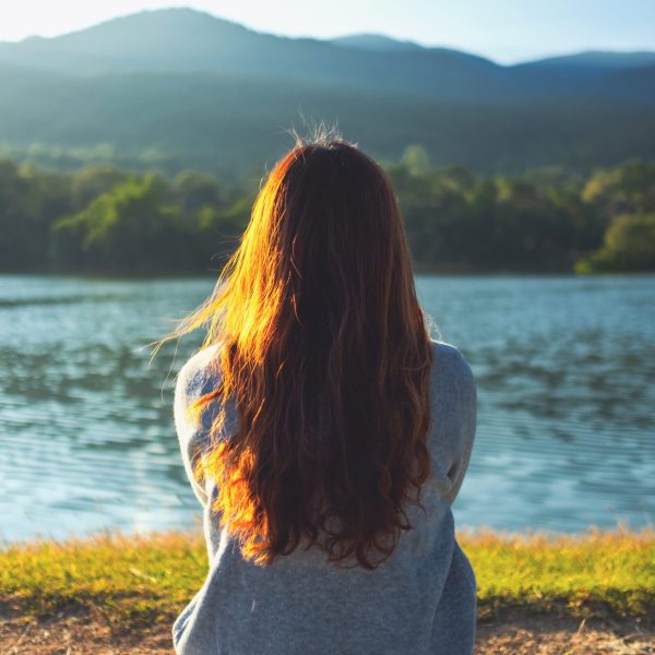 A woman sitting alone by the lake looking at the mountains with green nature background