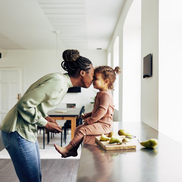 Loving young African mom and her cute little daughter eating a healthy fruit snack together in their kitchen at home